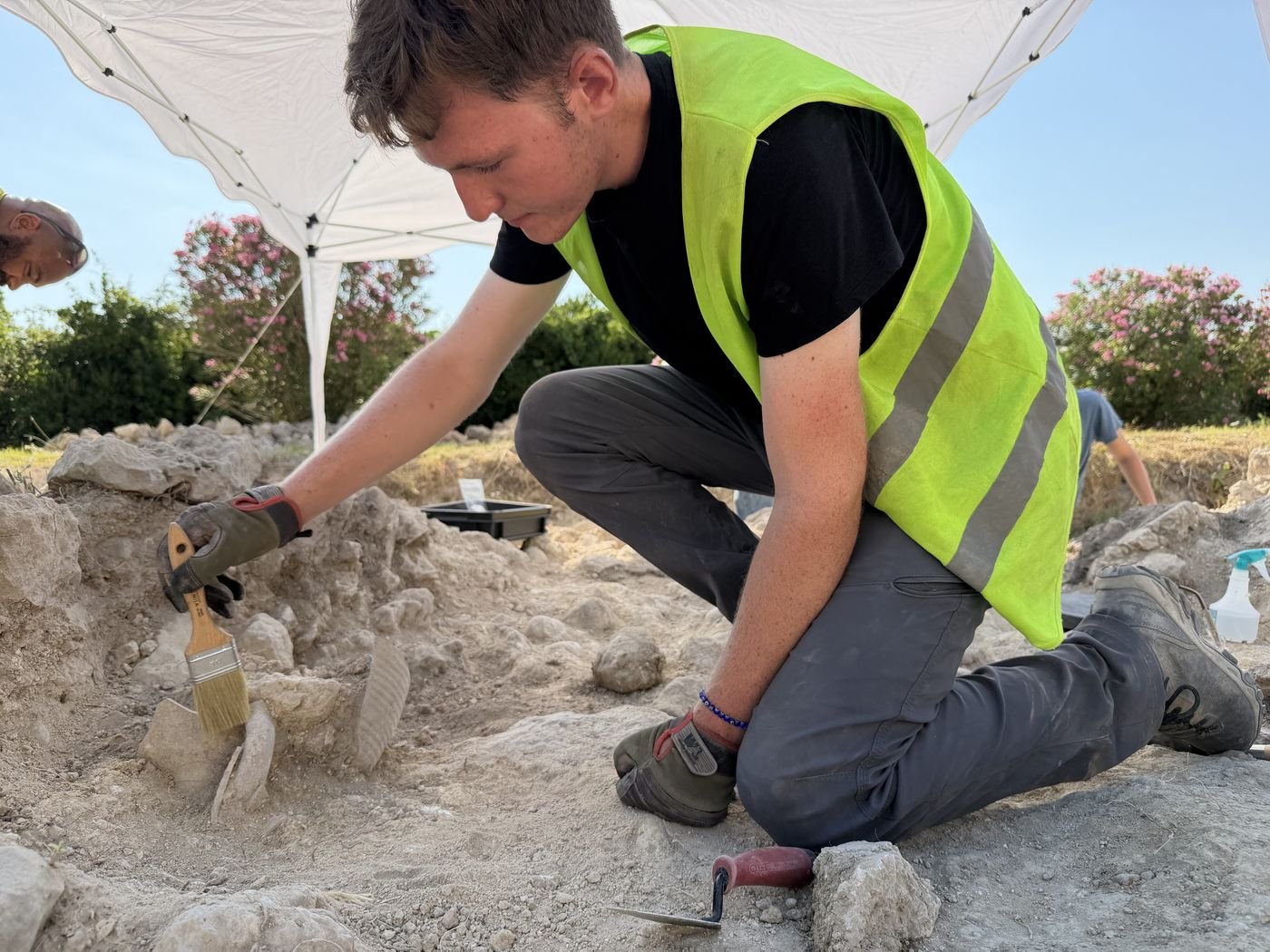 Brushing soil away from pottery fragments under a field tent